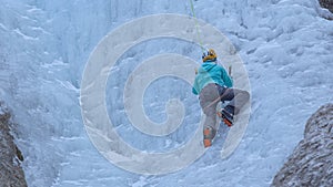 CLOSE UP: Woman with crampons and ice axes scales the gorgeous frozen waterfall.