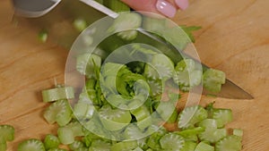 Close-up of a woman cutting fresh celery on a wooden chopping board.
