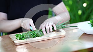 Close-up of woman cutting green onion on wooden board outdoors. Women's hands cutting verdure with knife on chopping