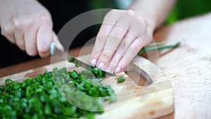 Close-up of woman cutting green onion on wooden board outdoors. Women`s hands cutting verdure with knife on chopping