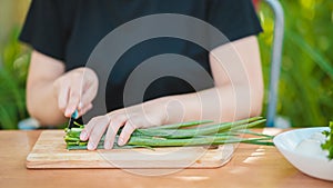 Close-up of woman cutting green onion on wooden board outdoors. Women`s hands cutting verdure with knife on chopping board