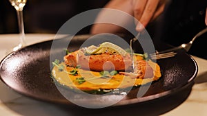 Close up of woman cutting grilled salmon with fork and knife on black plate