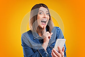 Close up of woman in denim jacket with smartphone over yellow background