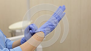 Close-up of a woman dentist`s hand putting on blue sterilized surgical gloves.