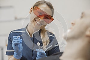 Close up of woman dentist smiling to a client and holding dental instruments.