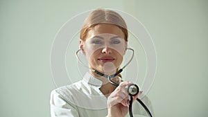 Close-up of woman doctor in white coat in clinic at workplace holds stethoscope in his hand and listens to breathing of