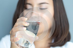 Close up woman drinking pure water from glass with blue background, Selective focus