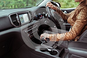 Close-up, woman driving a car includes a gearbox, reversing, starting to move in woods, leather jacket, automatic