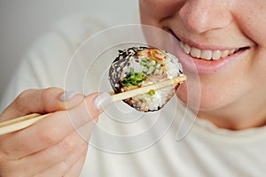 Close-up of woman eating sushi roll with chopsticks