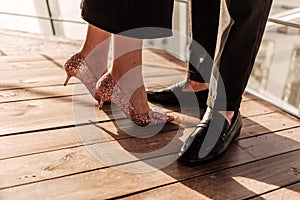 Close up a woman in elegant black dress and rose golden high heels staying together with her man in black pants and