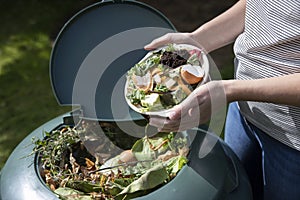 Close Up Of Woman Emptying Food Waste Into Garden Composter At Home