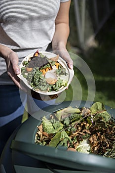 Close Up Of Woman Emptying Food Waste Into Garden Composter At Home