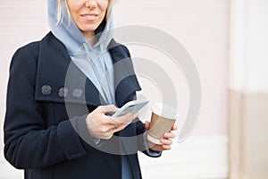 Close up of woman enjoying coffee to go and using her cellphone outdoors during break. Surfing the web internet in smartphone.