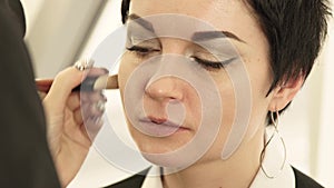 Close up woman face during applying makeup cosmetic with brush on skin in beauty salon. Portrait beautiful woman while