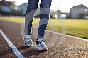 Close up of woman feet in sport sneakers and blue jeans on running lane on outdoor sports court