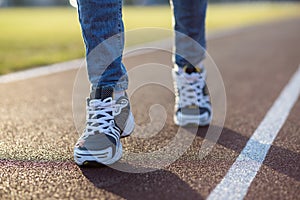 Close up of woman feet in sport sneakers and blue jeans on running lane on outdoor sports court