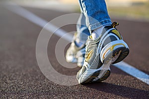 Close up of woman feet in sport sneakers and blue jeans on running lane on outdoor sports court