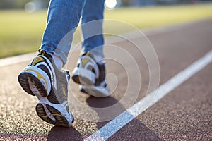 Close up of woman feet in sport sneakers and blue jeans on running lane on outdoor sports court