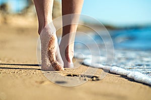 Close up of woman feet walking barefoot on sand leaving footprints on golden beach. Vacation, travel and freedom concept. People