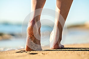 Close up of woman feet walking barefoot on sand leaving footprints on golden beach. Vacation, travel and freedom concept. People