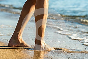 Close up of woman feet walking barefoot on sand leaving footprints on golden beach. Vacation, travel and freedom concept. People