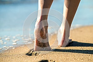 Close up of woman feet walking barefoot on sand leaving footprints on golden beach. Vacation, travel and freedom concept. People