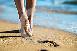 Close up of woman feet walking barefoot on sand leaving footprints on golden beach. Vacation, travel and freedom concept. People