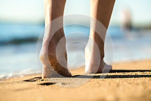 Close up of woman feet walking barefoot on sand leaving footprints on golden beach. Vacation, travel and freedom concept. People