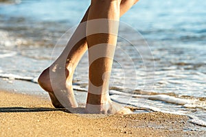 Close up of woman feet walking barefoot on sand leaving footprints on golden beach. Vacation, travel and freedom concept. People