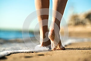 Close up of woman feet walking barefoot on sand leaving footprints on golden beach. Vacation, travel and freedom concept. People