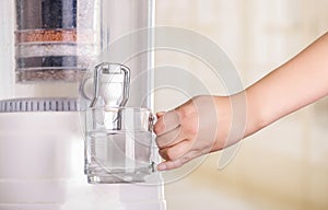 Close up of a woman filling a glass of water, with a filter system of water purifier on a kitchen background