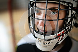 Close-up of woman floorball goalkeeper in helmet concetrating on game in gym.