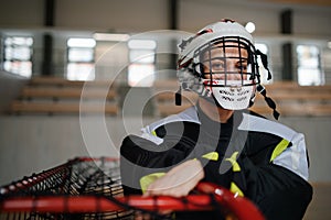 Close-up of woman floorball goalkeeper in helmet concetrating on game in gym.