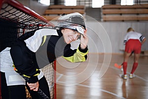 Close-up of woman floorball goalkeeper in helmet concetrating on game in gym.