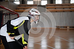 Close-up of woman floorball goalkeeper in helmet concetrating on game in gym.