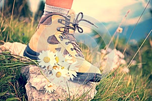 Close up of a woman foot in a hiking shoe and a bunch od daisies on a mountain trail