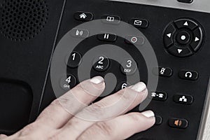 A close up woman hand dialing, a Black office IP Phone on a desk