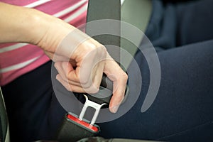 Close up of woman hand fastening seat belt while sitting inside a car for safety before driving on the road. Female driver driving