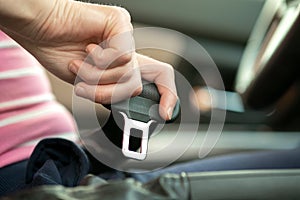 Close up of woman hand fastening seat belt while sitting inside a car for safety before driving on the road. Female driver driving