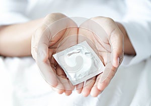 Close up woman hand holding condom lying on white bed, health care and medical concept