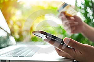 Close up woman hand holding credit card, using smart phone outdoor for online shopping while working on laptop