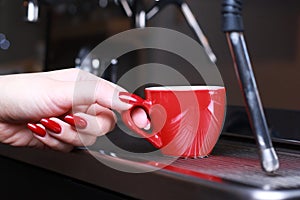 Close-up, a woman hand holding a cup of coffee mugs is standing in the coffee maker, the background is blurred