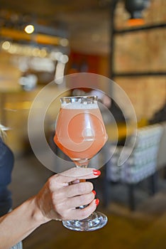 Close up of woman hand holding glass of draft lager beer. Fruit beer in a glass. Eating out in restaurant concept