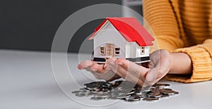 Close up woman is hand holding house model over coins stack. Concept for property ladder mortgage and real estate