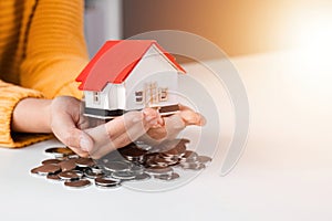 Close up woman is hand holding house model over coins stack. Concept for property ladder mortgage and real estate