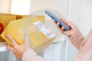 Close up of woman hand holding mobile phone and scaning product box for delivering to customer, online shopping, small business