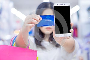 Close up woman hand holding phone, shopping bag and credit card in the shopping mall. Shopping concept