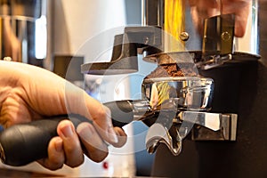 Close up woman hand holding portafilter, girl barista is grinding the roasted coffee beans into powder using coffee grinder at