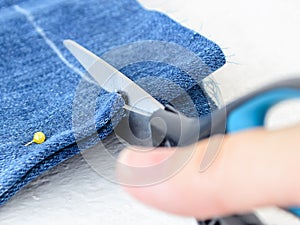 Close-up of woman hand holding a scissors and cutting out folded in half blue jean shorts. DIY shorts out of jeans