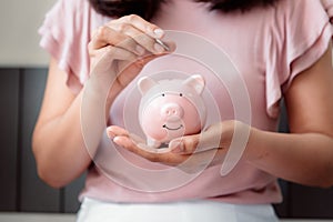 Close-Up Woman Hand is Putting a Money Coin into Piggy Bank on The Bedroom., Female Hand is Inserting Coin in Pink Piggy Saving.